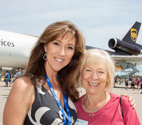 women taking photo standing in front of plane at EAA AirVenture Oshkosh